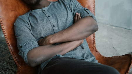 Handsome African man with the beard is sitting in the chair and smiling. A male looks dreamy, thoughtful and calm.の写真素材