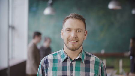 Portrait of young successful businessman at busy office. Handsome male employee looking at camera and smiling.の写真素材