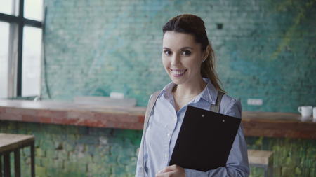 Portrait of young successful caucasian woman looking at camera and smiling. Female holds the documents at modern office.の写真素材