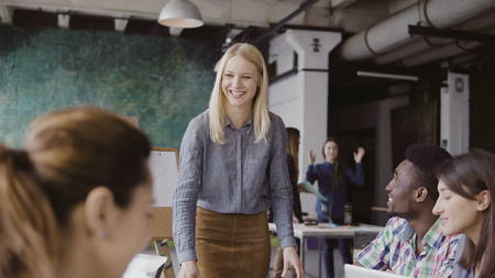 Beautiful blonde woman manager giving direction to multiethnic team. Creative business meeting at modern hipster office.の写真素材