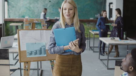 Female blonde manager comes to young business team. Multiracial group of people meeting in trendy hipster office.の写真素材