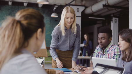 Blonde woman team leader giving direction to mixed race team of young guys. Creative business meeting at modern office.の写真素材