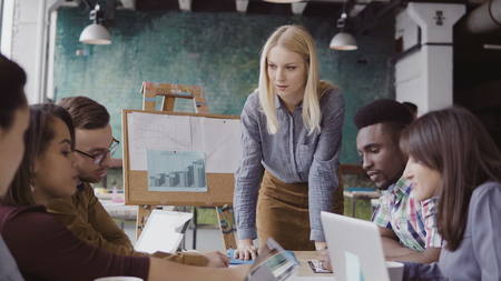 Blonde woman team leader giving direction to mixed race team of young guys. Creative business meeting at modern office.の写真素材