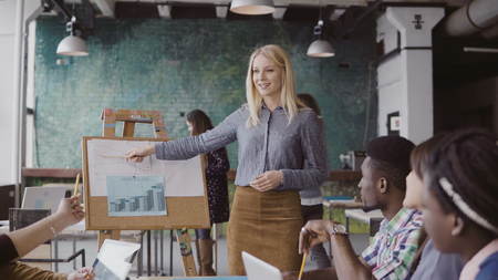 Young blonde female manager motivates mixed race colleagues to work. Team leader presents financial data at loft office.の写真素材