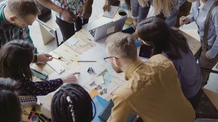 Top view of young team working on new project. Group of mixed race people standing near the table and discussing.の写真素材
