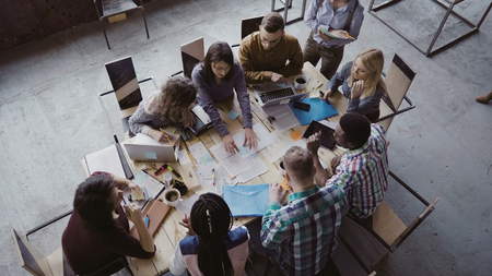Top view of mixed race business team sitting at the table at loft office and working. Woman manager brings the document.の写真素材