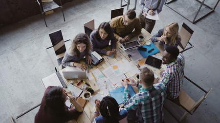 Business meeting at loft shared space. Multiethnic team talking, woman manager giving direction to people. Top view.の写真素材