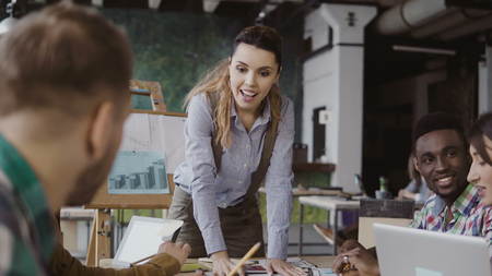 Brunette female team leader talking with mixed race group of people, writes with a marker on the model of house.の写真素材