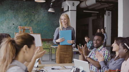 Close-up view of female manager walking through the office with documents. Multiracial team clap to businesswoman.の写真素材