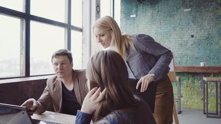 Young blonde team leader walking through modern office and controls work of employee. Female looks the fabric examples.の写真素材