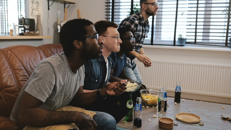 Mixed race male supporters watch sports on TV. Fans celebrate goal victory holding British flag cushion. Slow motion.の写真素材