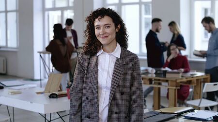Medium shot portrait of happy positive young Caucasian business woman with curly hair smiling at...
