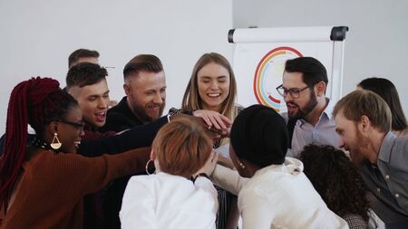 Happy multiethnic business people join hands to celebrate business success with young male boss....