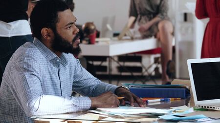 Happy young African man in formal clothes taking a job interview sitting at busy modern office table. Healthy workplace.の写真素材