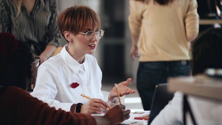 Medium portrait of happy successful young European business woman in eyeglasses at multiethnic modern office meeting.の写真素材