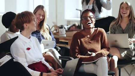 Happy young multiethnic business women sit together listening to corporate seminar laughing at modern office conference.の写真素材