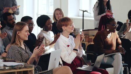 Happy smiling young multiethnic audience applause to speaker after conference seminar at modern office training meeting.の写真素材