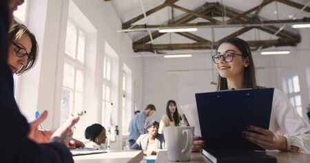 Elegant young confident team leader woman in glasses giving instructions to multiethnic colleagues in modern office.の写真素材