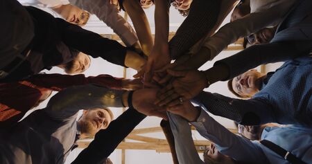 Low angle close-up, happy group of diverse business people put hands together. Teamwork at modern...