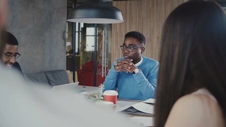 Handsome African American young manager discussing work with multiethnic colleagues at team meeting...