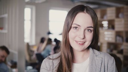 Happy beautiful Caucasian young manager smiling at camera. Portrait of positive female boss posing in modern office 4K.の写真素材