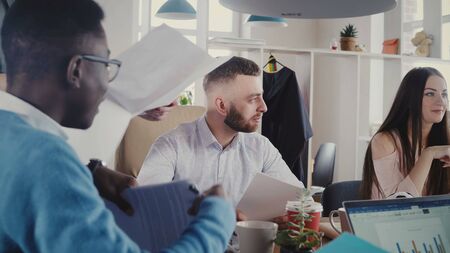 Happy multiethnic business people meeting in office. Female manager gives documents to employees at...