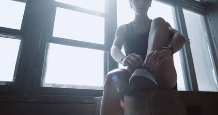 Young beautiful athletic blonde woman tying sneaker shoe laces, resting after intense power workout in gym slow motion.の写真素材