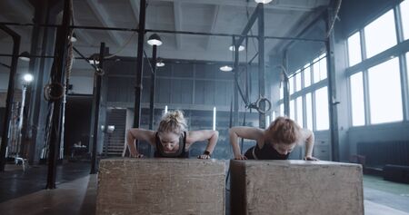 Happy beautiful young blonde woman working out together with personal female coach in big gym doing...