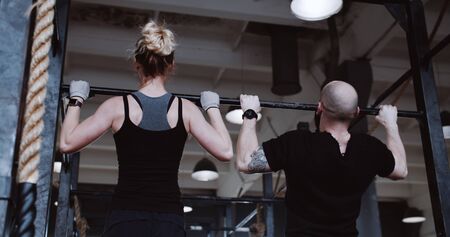 Back view young athletic Caucasian man and woman working out doing pull-ups slow motion. Healthy...