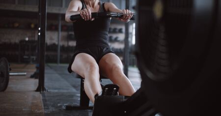 Beautiful young successful blonde woman working out on stationary rowing machine in gym. Healthy...