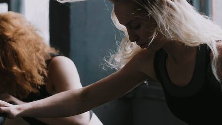 Two young smiling athletic European women work out on gym bicycle machines during cardio training, slow motion.の写真素材