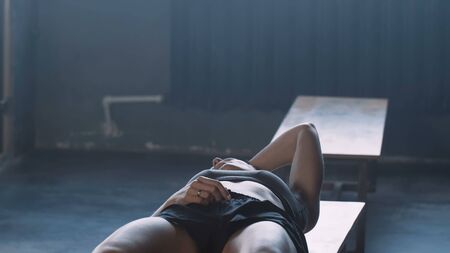 Young beautiful blonde athlete woman lying down alone in dark gym locker room, feeling lost and stressed under pressure.の写真素材