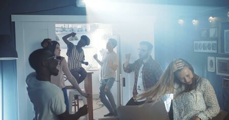 Happy excited multiethnic young college students dance together at party with lights, celebrating holidays slow motion.の写真素材