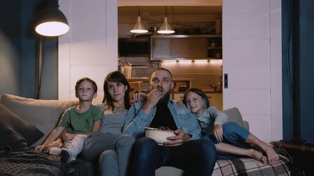 Happy positive young Caucasian family with children watch movies expressing different emotion at home on couch together.の写真素材