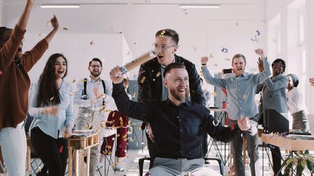 Happy middle aged boss celebrates success with team and confetti at multiethnic healthy office slow motionの写真素材