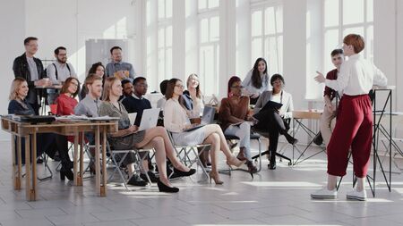 Group of happy multiethnic business people listen to female coach speaking at modern office seminar slow motionの写真素材
