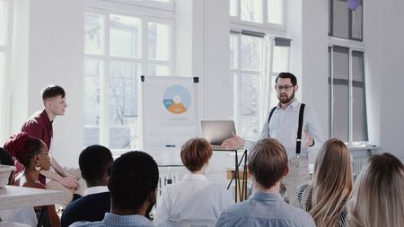 Young skilled businessman coach giving a talk before small audience at modern light office seminarの写真素材