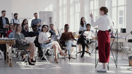 Young short haired business woman giving seminar talk at modern office, multiethnic team clapping slow motion.の写真素材