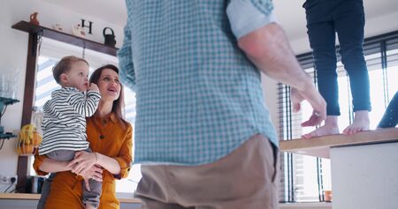 Happy young Caucasian mother and father playing with cute little sons in house kitchen, family fun concept slow motion.の写真素材
