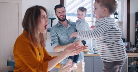 Happy young Caucasian mother and father playing with two little sons in the kitchen, family fun time at home slow motionの写真素材