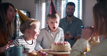 Little happy Caucasian boy child making wish, blow on birthday cake at surprise family party with confetti slow motion.の写真素材