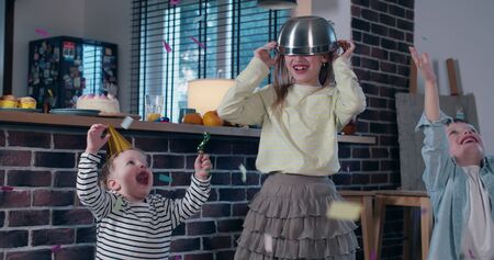 Cute happy teenage girl throwing confetti in the air celebrating birthday party with two little brothers slow motion.の写真素材