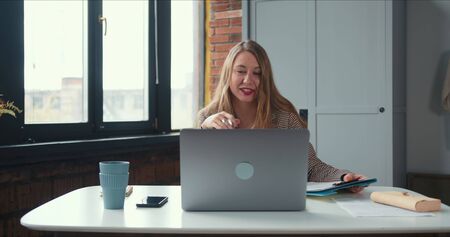 Work from home. Tilt down on young blonde boss woman in pajamas pants working online using laptop...