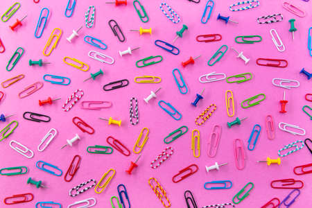 Colored paper clips are scattered on the background of pink flowersの写真素材