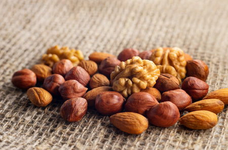Hazelnuts, walnuts, and almonds lie on a factory-made sackcloth. Nuts are a high-calorie and healthy...
