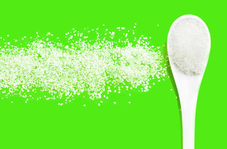 Sugar. A spoon with sugar on a green background. Caloric ingredient for baking and sweets