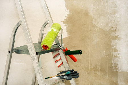 Stepladder, paint roller, brush, work gloves on the background of a concrete wall. Construction and painting worksの写真素材