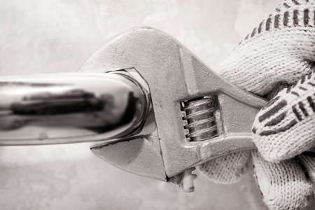 A wrench. Repair of a water tap. The hand clamps the nut with a wrench. Plumbing worksの写真素材