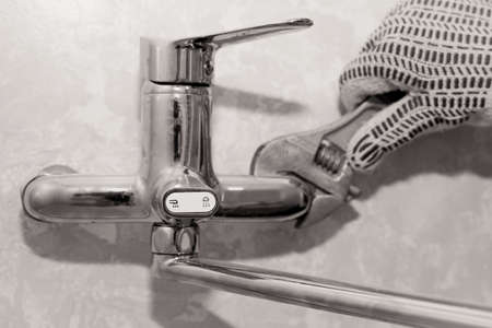 A wrench. Repair of a water tap. The hand clamps the nut with a wrench. Plumbing worksの写真素材