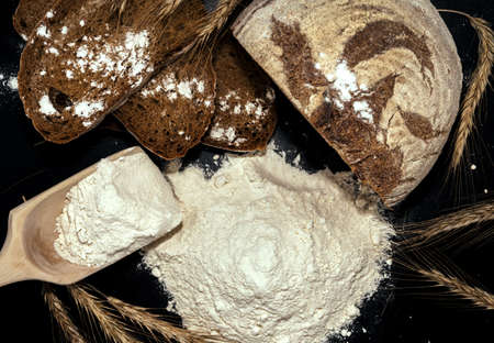 Bread, flour, spikelets of wheat on a black background. Flour is the main ingredient for baking.